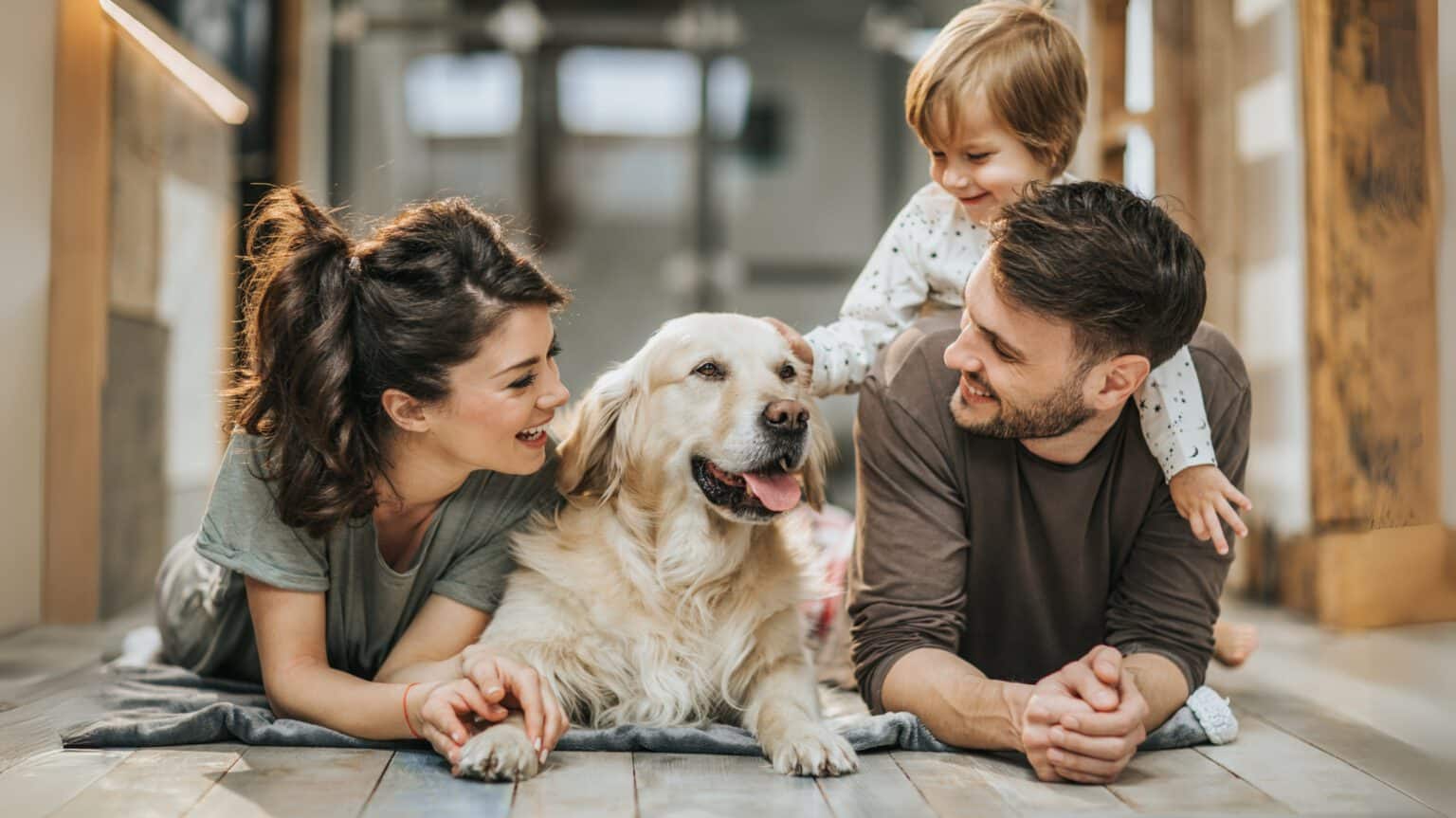 Geschützt durch Hundeversicherung - Familienhund liegt mit Familie auf dem Boden – HanseMerkur Hundeversicherung