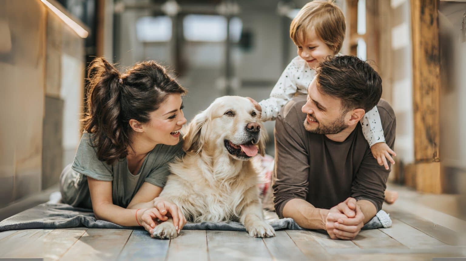 Geschützt durch HanseMerkur Hundeversicherung - Familie lacht mit Hund auf dem Boden – HanseMerkur Hundeversicherung
